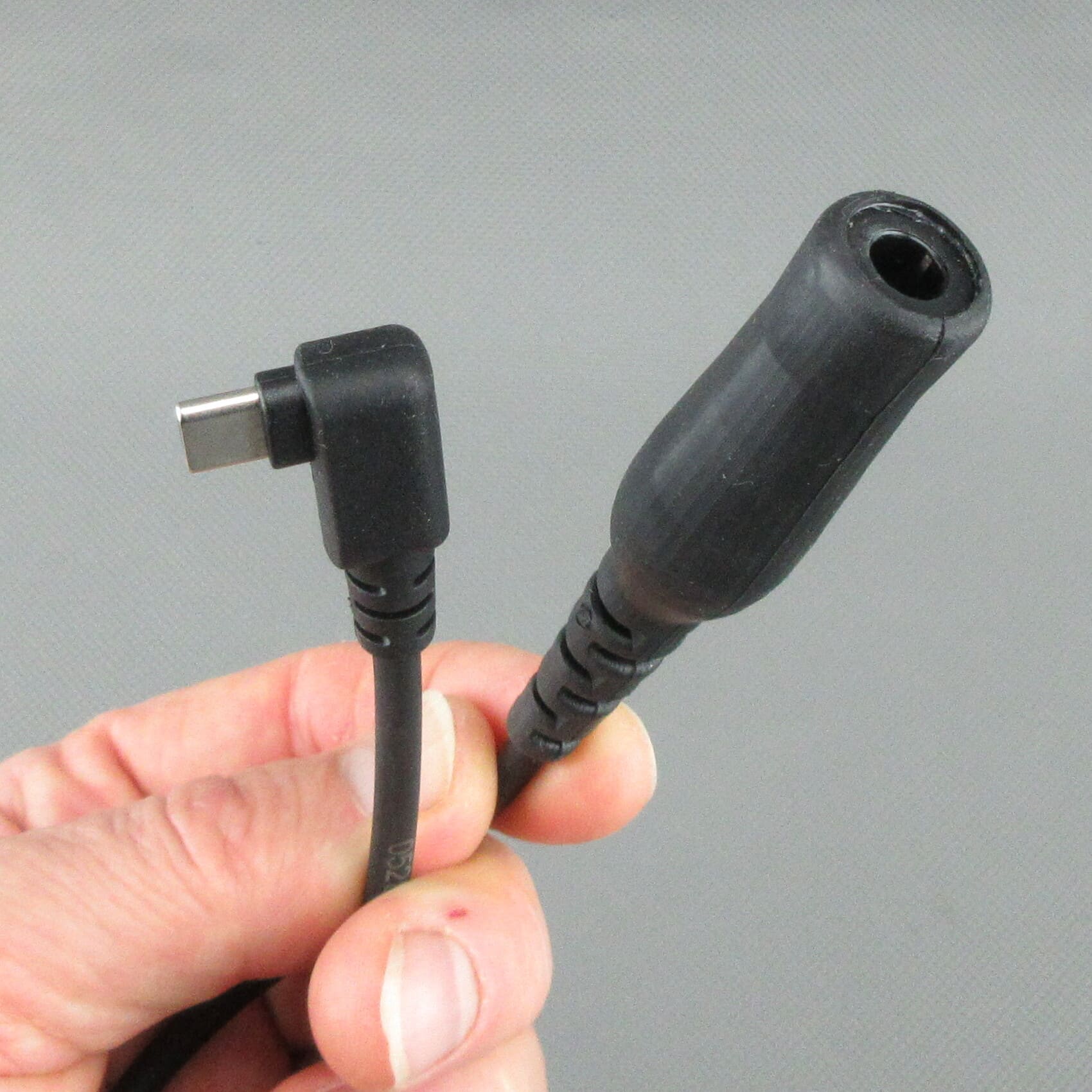 Mano che tiene il cavo adattatore StarCom1 FLX2, con il fuoco sul connettore USB-C angolato e sulla presa femmina TP-120 (compatibile Nexus® / Amphenol®) per il collegamento di cuffie tattiche con cablaggio NATO.