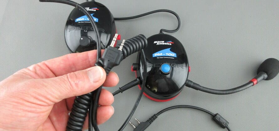 Cuffie MicroAvionics® con cavo di collegamento radio, che mostrano lo spinotto della radio tenuto in mano.